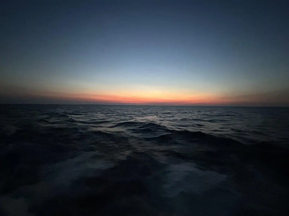 Dark rippling water beneath a low horizon glowing orange and pink at dawn.