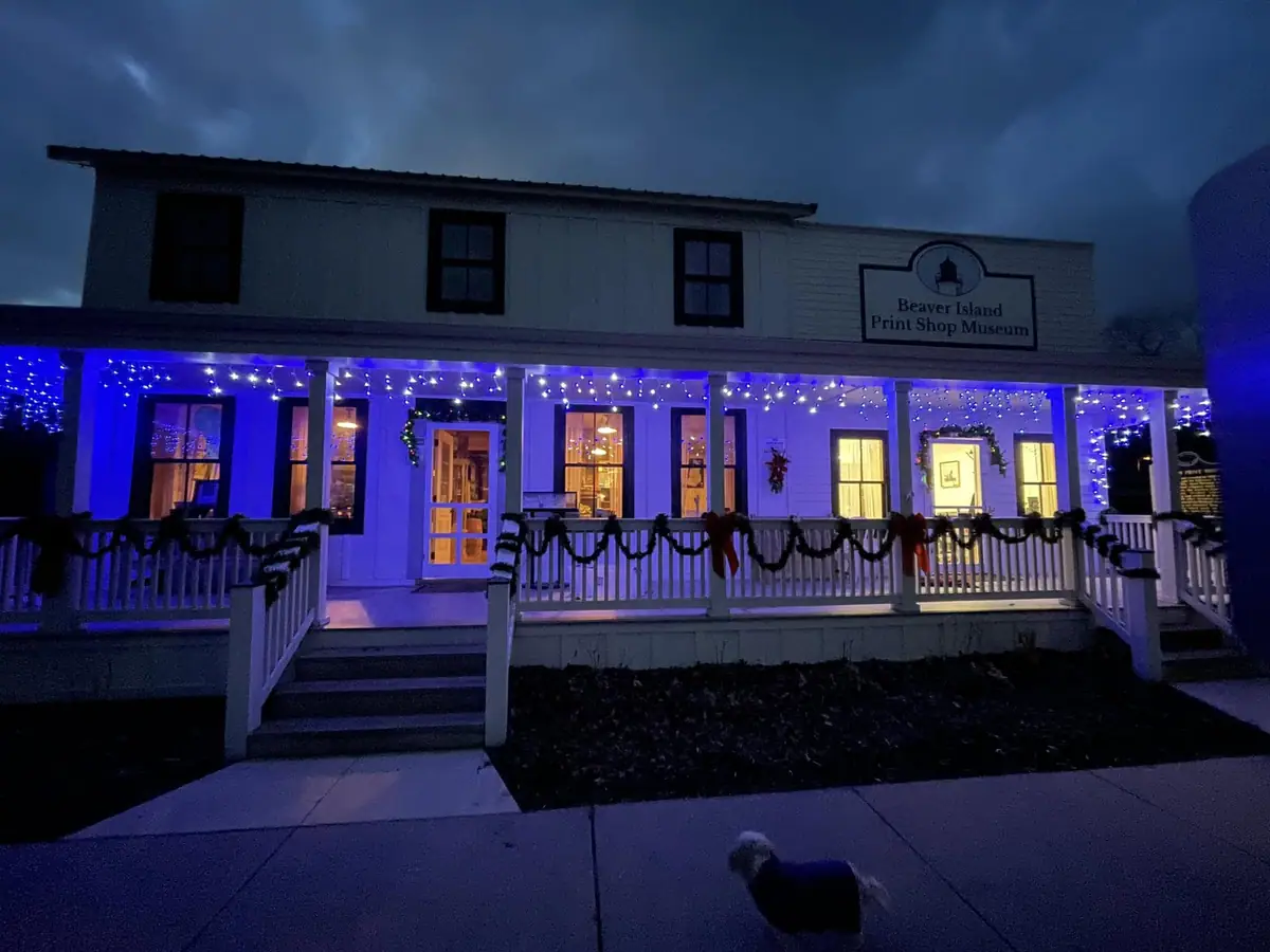 A white-fronted building glows with blue holiday lights at night, with a small dog on the sidewalk.