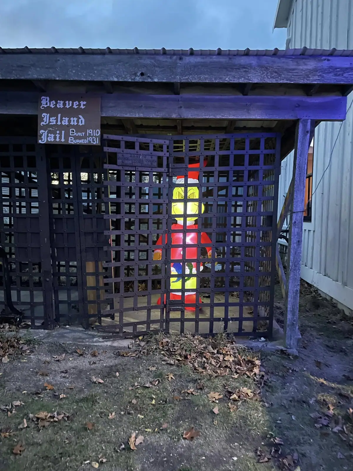 A barred wooden jail enclosure contains a colorful red-and-yellow figure beside a sign.