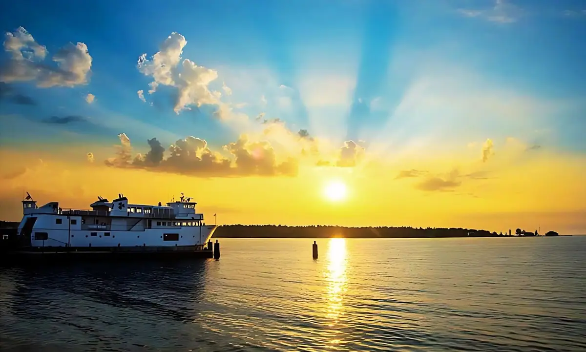 A white ferry rests beside a pier as the setting sun reflects across calm water.