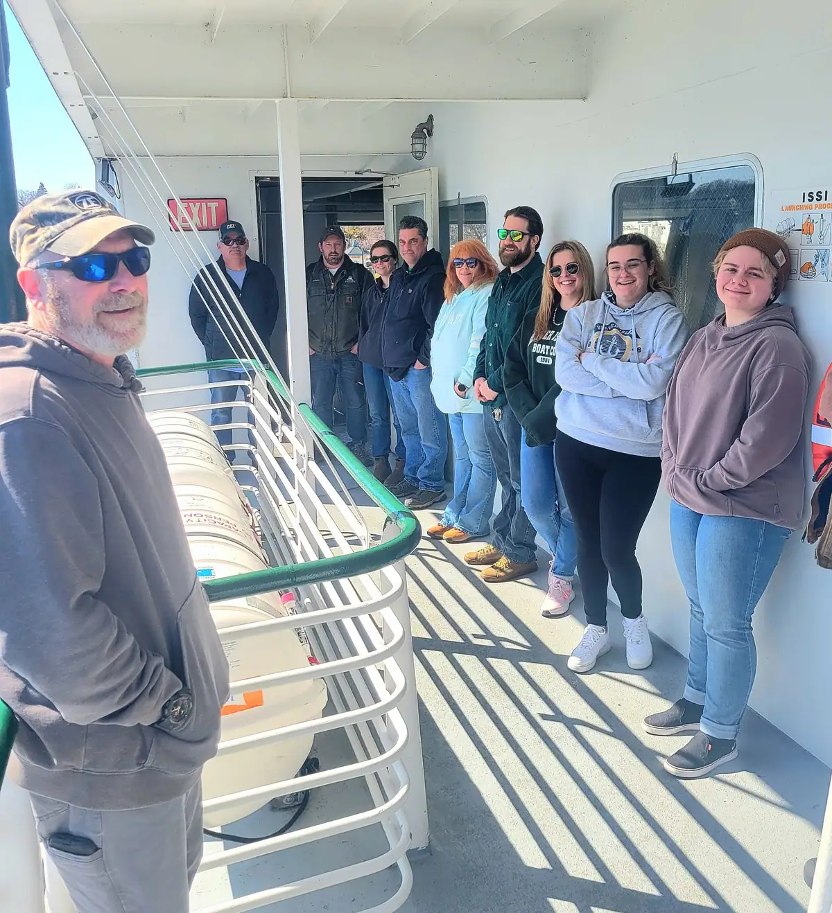 A group of people poses together on the covered deck of a passenger ferry.