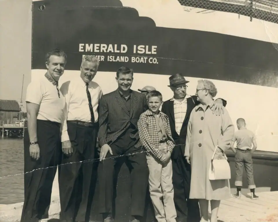 Six people pose on a dock beside the large vessel EMERALD ISLE, with another person visible near the stern.