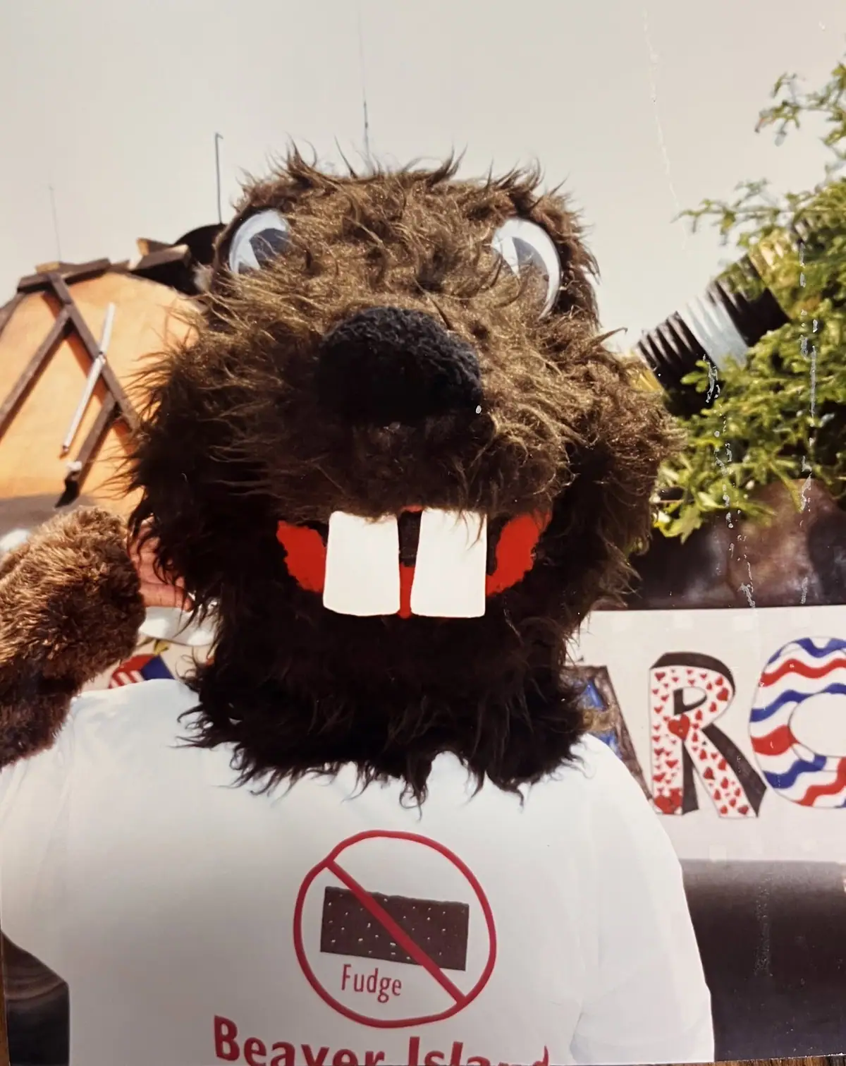 A person in a furry brown animal costume wears a white shirt with a crossed-out fudge graphic.