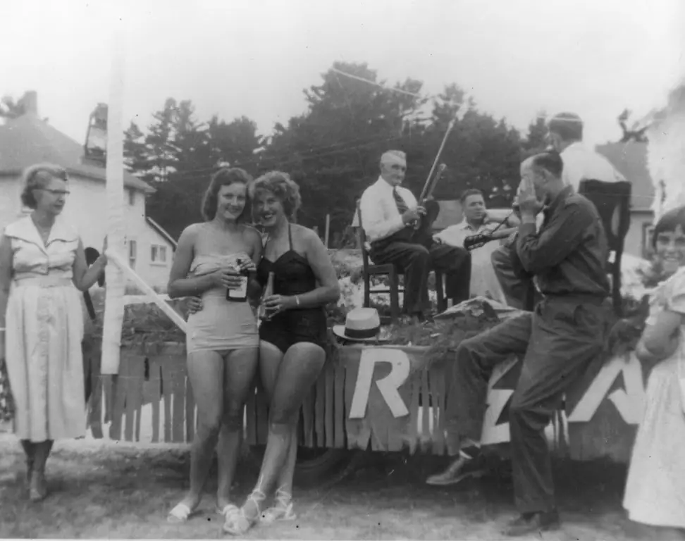 Black-and-white photograph of people gathered outdoors, including two women in swimsuits and seated musicians.