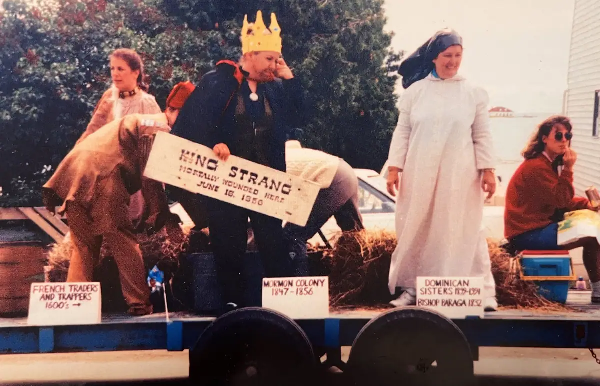 Costumed people ride on a parade float displaying signs about local historical figures and communities.