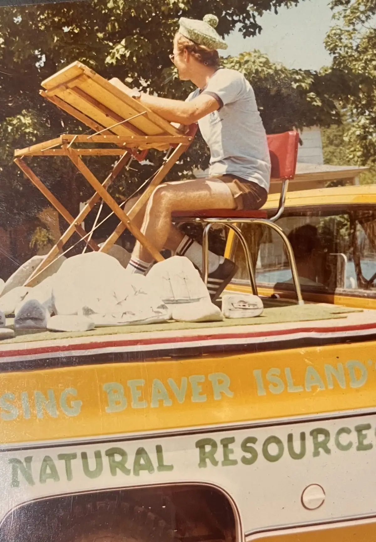 A person works at a folding table on the deck of a yellow boat with painted lettering.