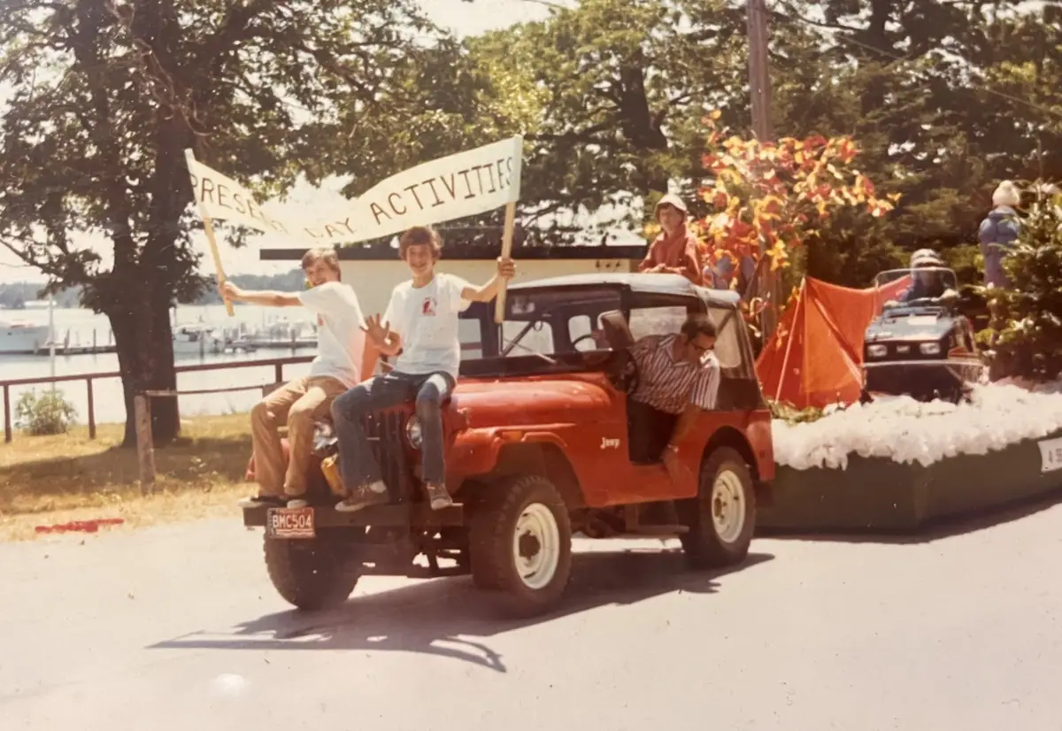 A red Jeep carries people and a decorated float with a sign reading “PRESENT DAY ACTIVITIES.”
