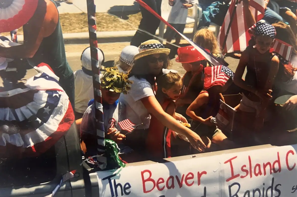 Children in patriotic costumes ride on a decorated parade float with hand-painted lettering.