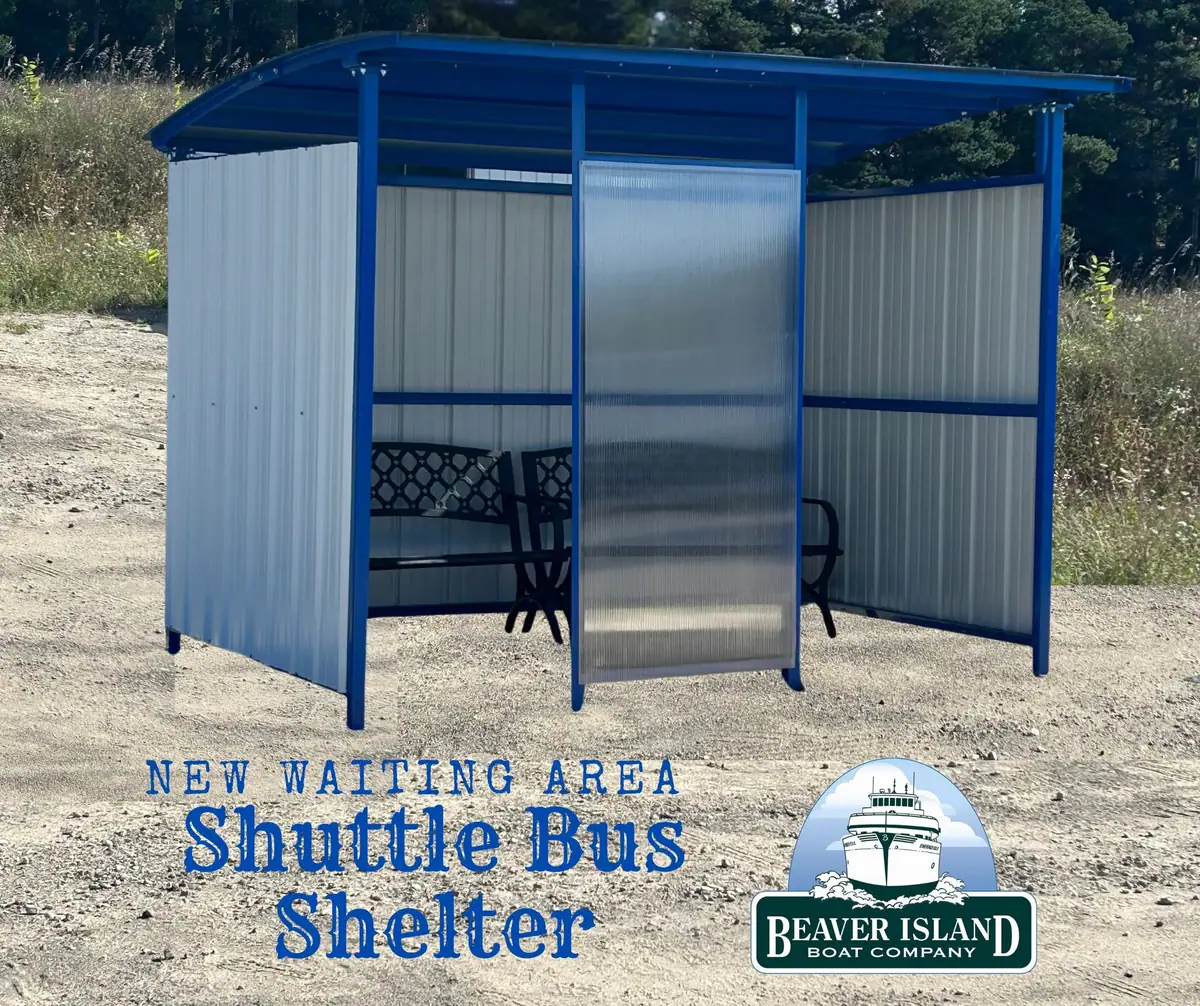 A blue-framed shelter with corrugated walls, a bench, and a translucent door stands beside a gravel area.