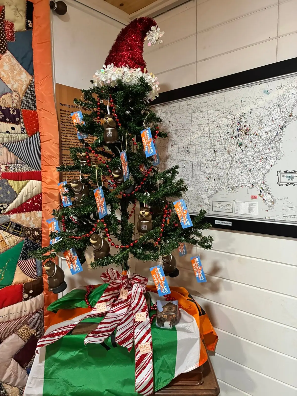 A decorated Christmas tree stands beside a wall map and a patchwork quilt.