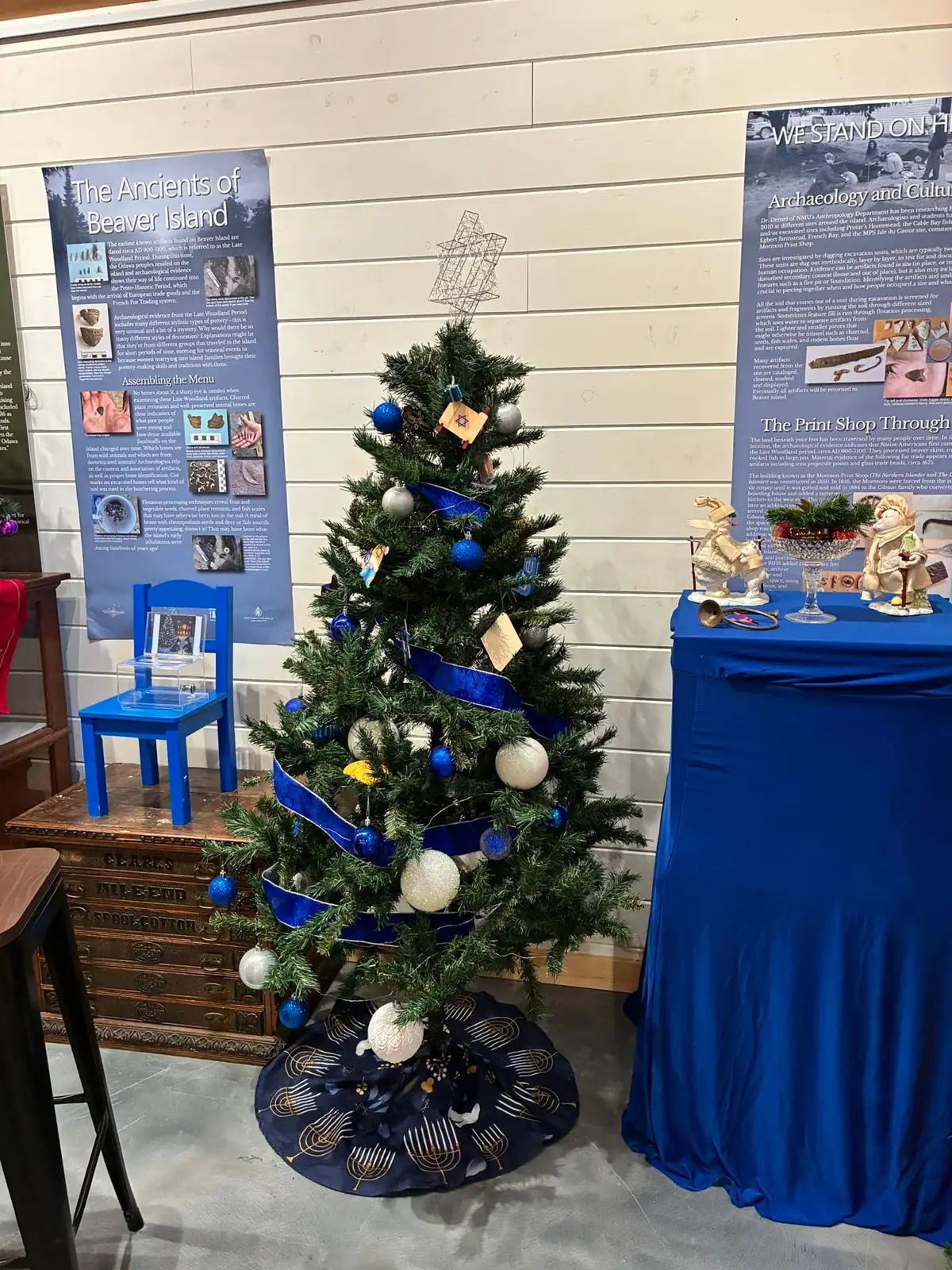 A small decorated holiday tree stands among museum exhibit panels and display tables.