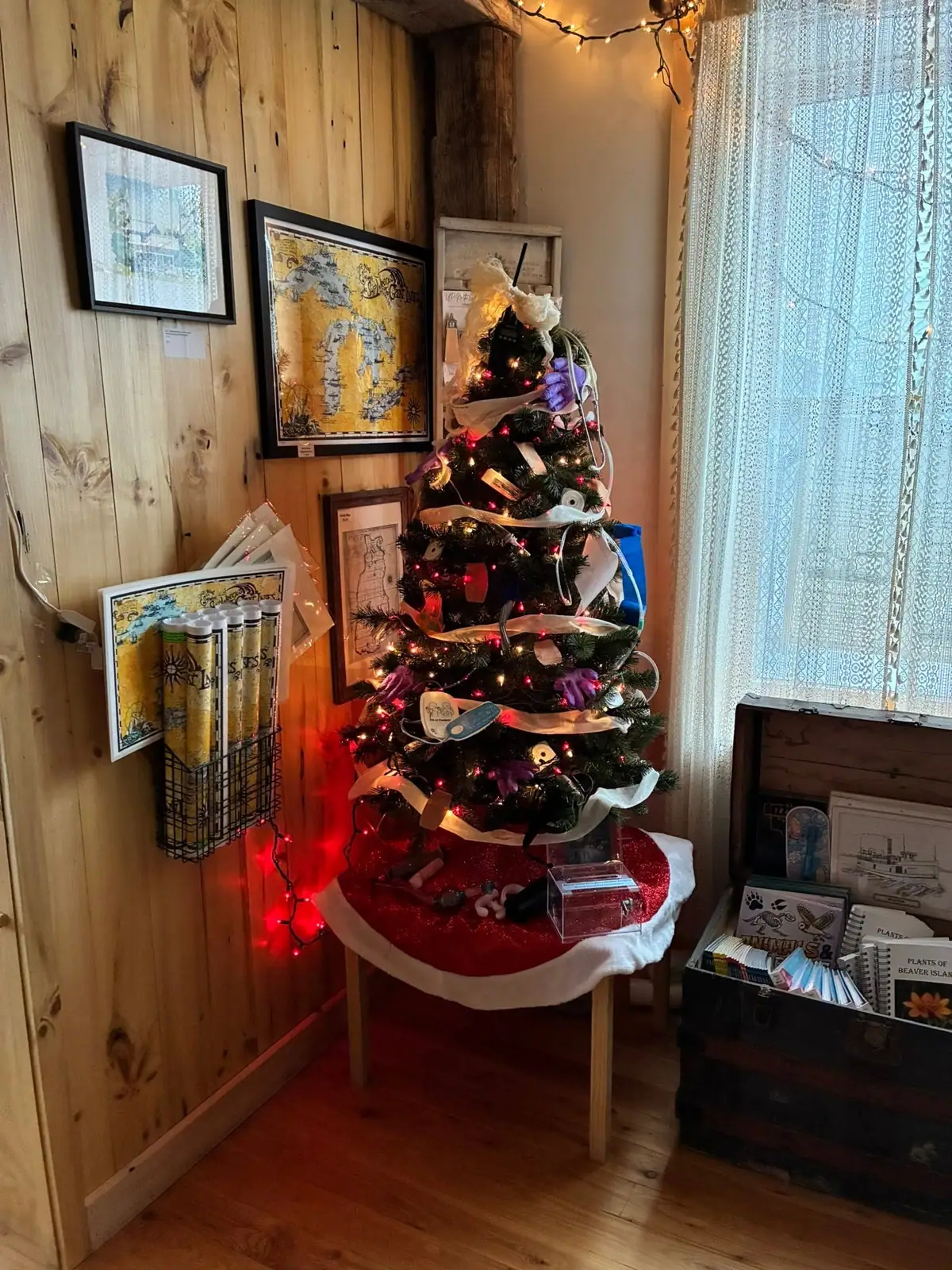 A decorated Christmas tree stands among framed maps and printed materials in a wood-paneled room.