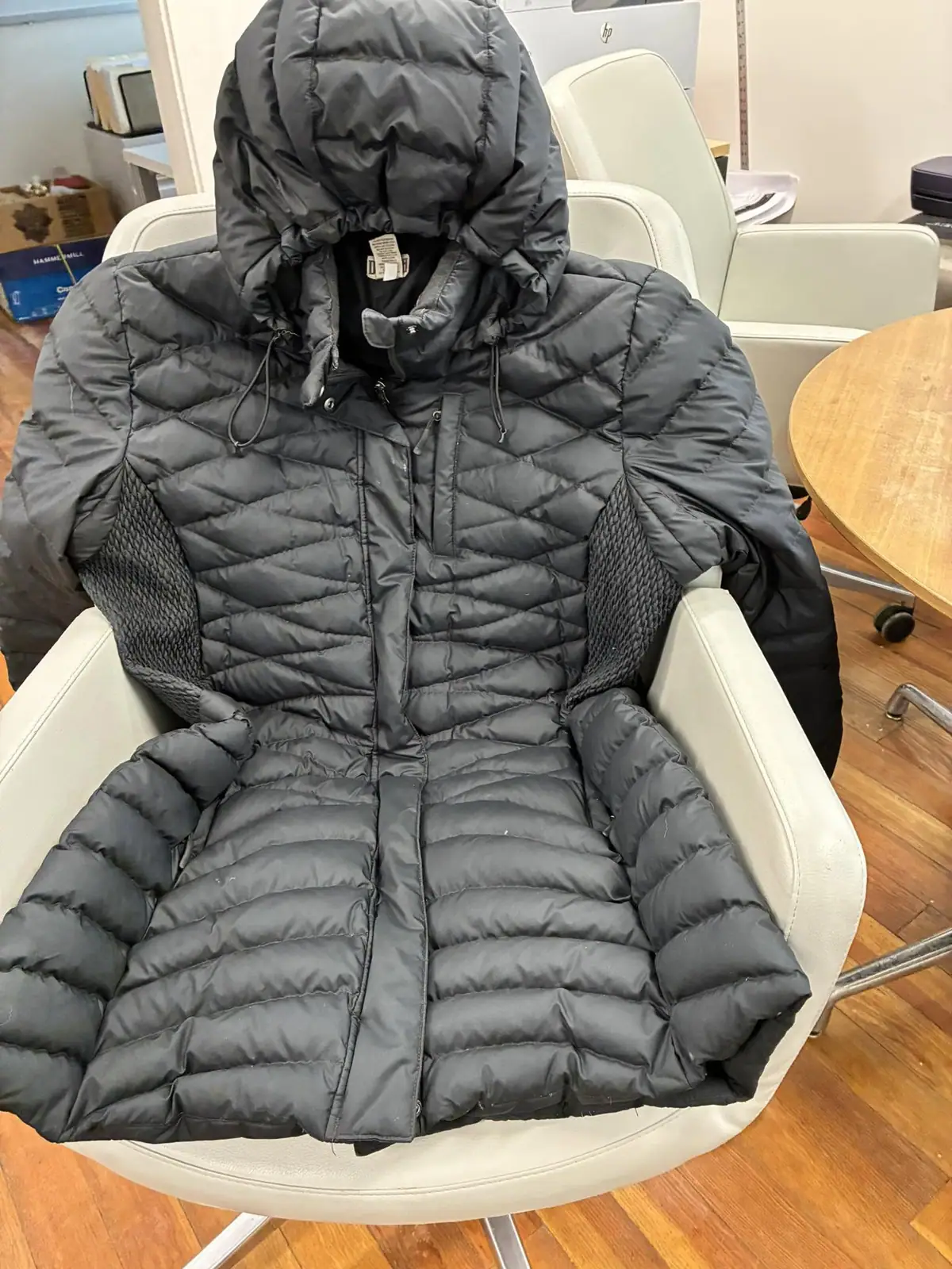 A dark quilted hooded coat is spread across a white office chair.