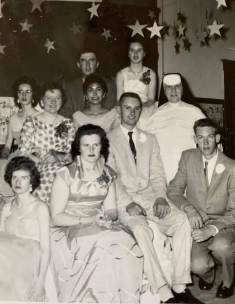 Black-and-white group portrait of eleven people in formal clothing beneath hanging star decorations.