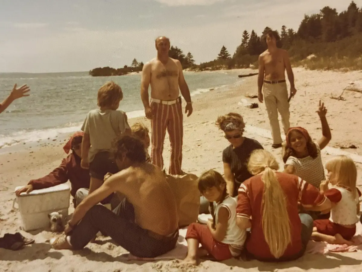 A group of adults and children gathers on a sandy beach beside the water.