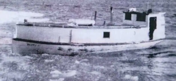Black-and-white photograph of a small white workboat moving through choppy water.