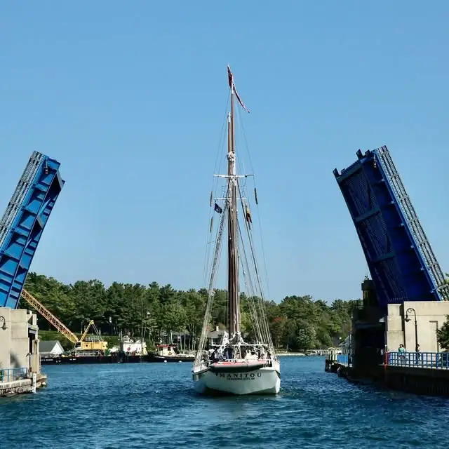 A sailboat passes between two raised blue drawbridges on a sunny day.