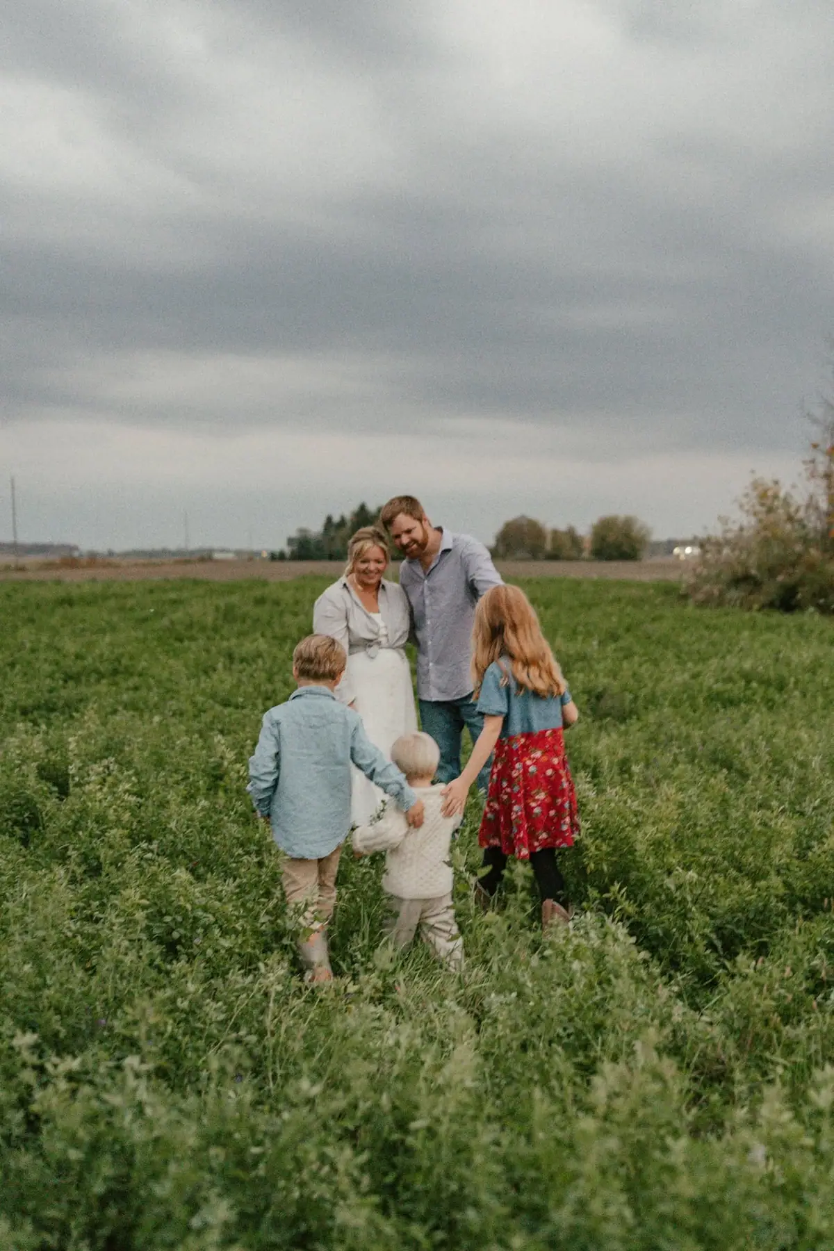 Five people walk together through a green field beneath a cloudy sky.