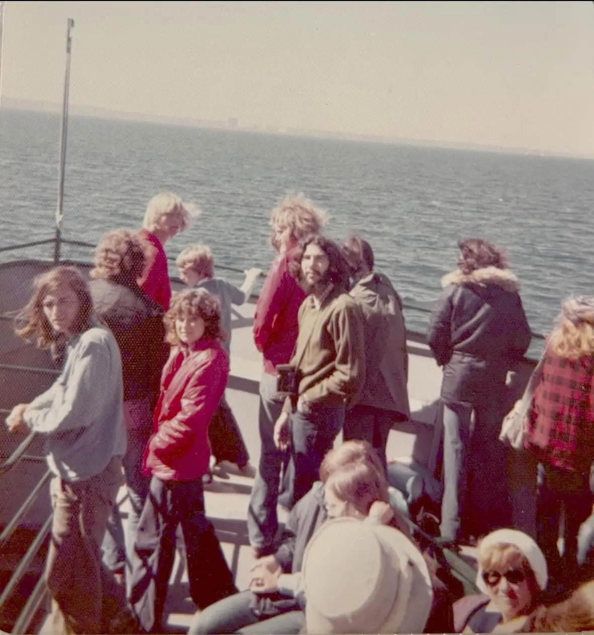 A group of passengers gathers on the open deck of a vessel above rippling water.