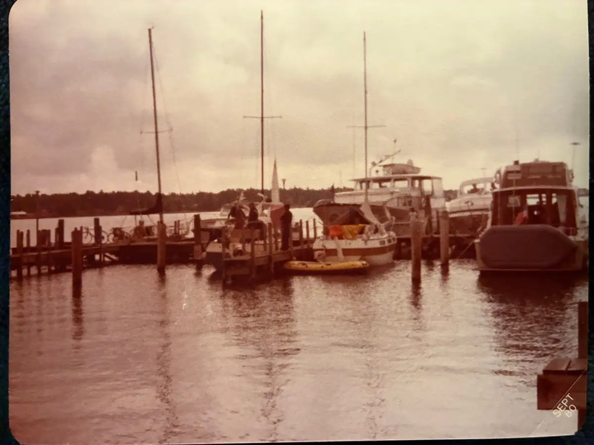 Sepia-toned harbor scene with sailboats, motorboats, a pier, and people under an overcast sky.