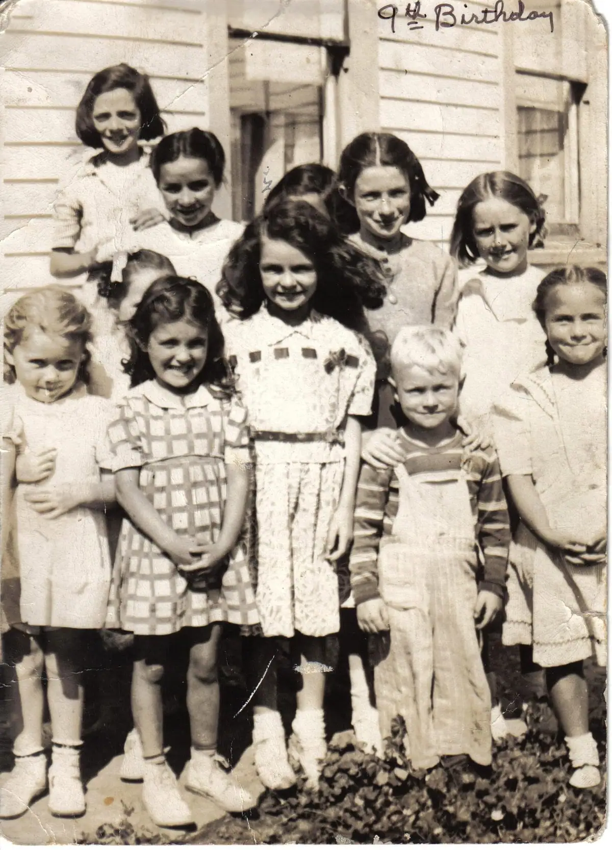 Children pose outdoors before a wood-sided house, with a handwritten “9th Birthday” inscription above them.