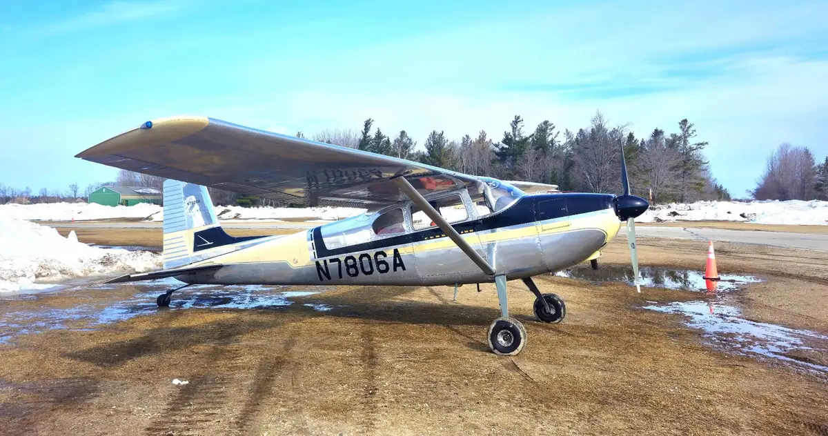 A light aircraft marked N1806A is parked on a snowy airfield beside a traffic cone.