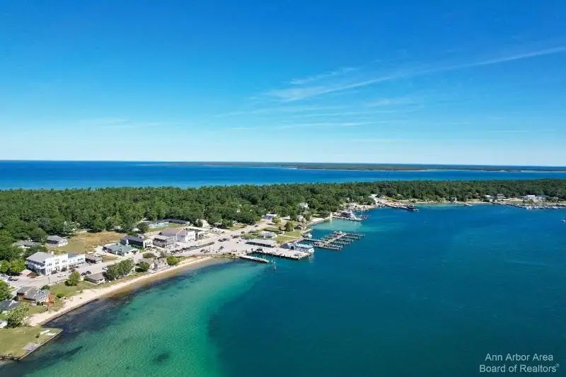 Aerial view of a wooded shoreline settlement with docks, beaches, roads, and buildings beside blue water.
