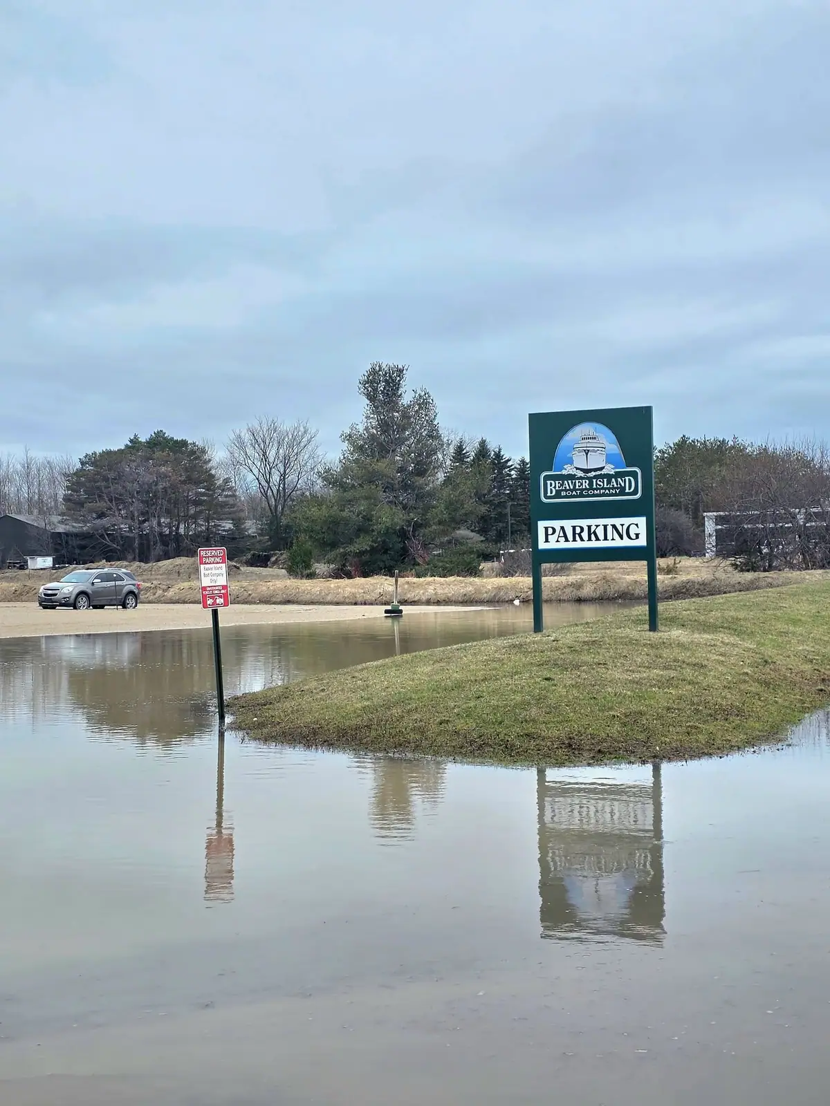 Floodwater surrounds a parking sign beside a partially submerged roadway.