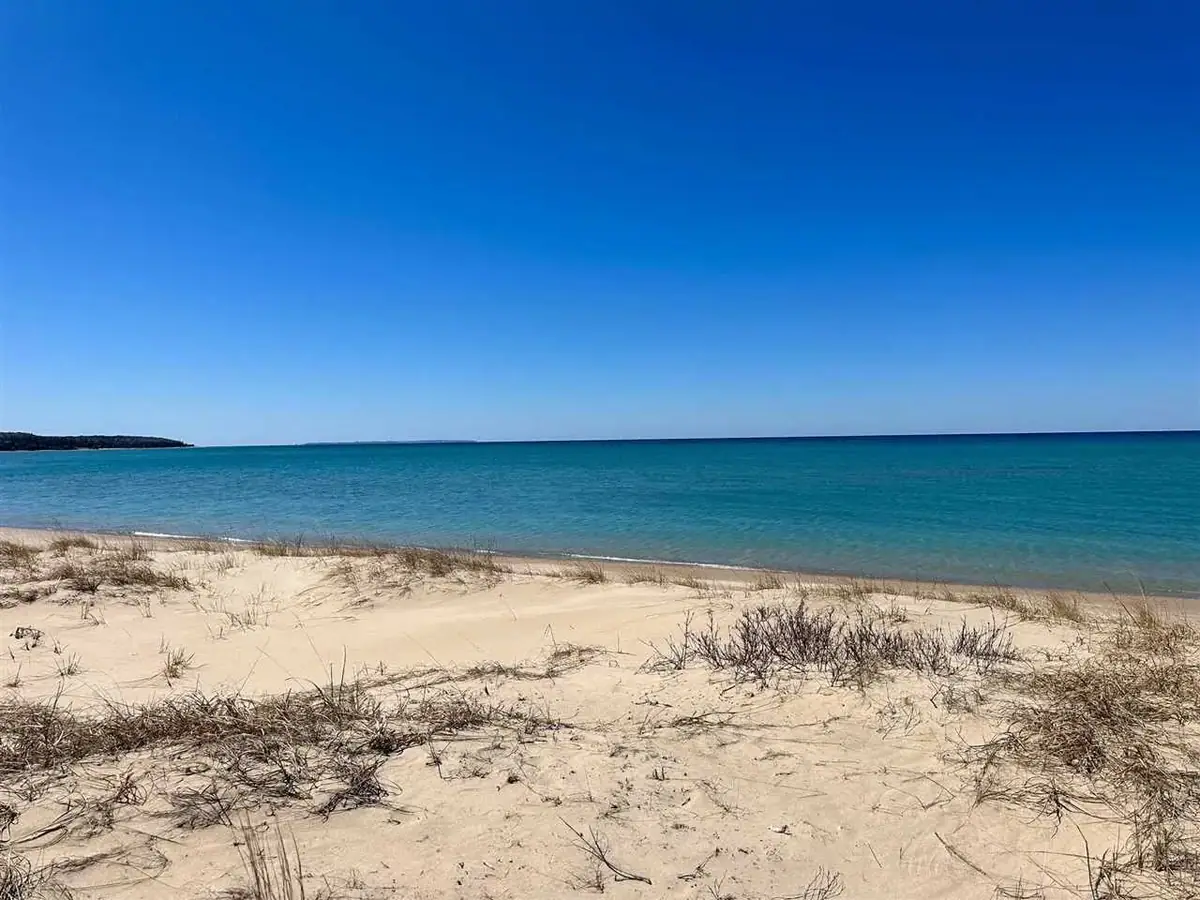 A sandy beach with sparse dune vegetation borders bright turquoise water beneath a clear blue sky.
