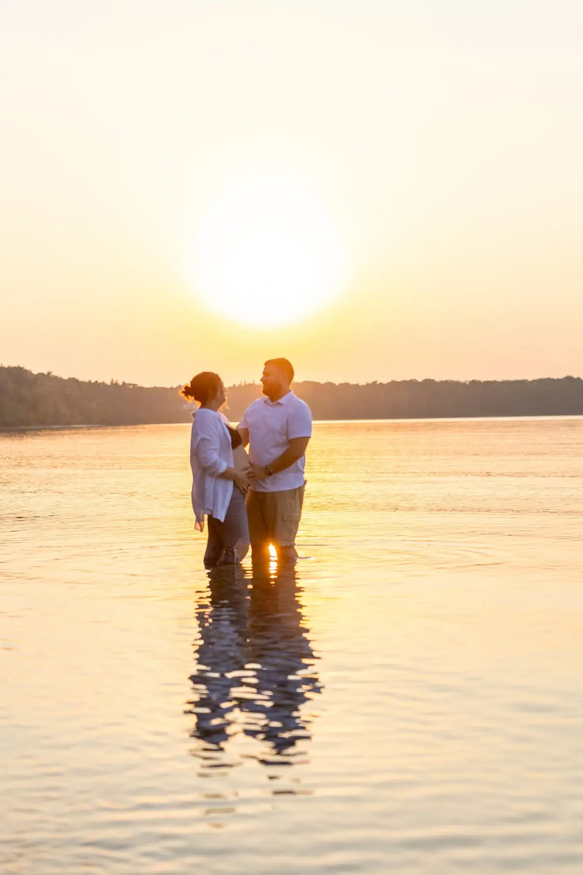 Two people stand hand in hand in shallow water at sunset.