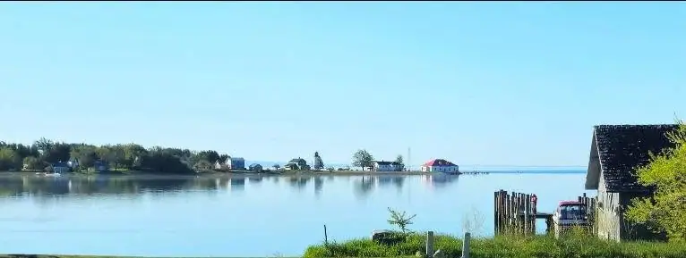 A calm waterfront with houses across the water and a weathered wooden building in the foreground.