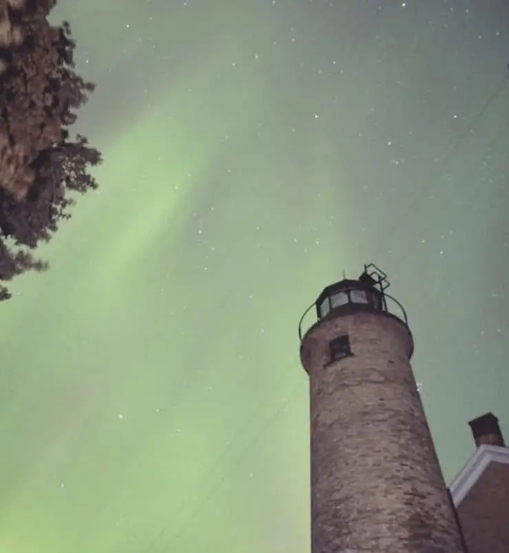 A brick lighthouse tower rises beneath stars and a faint green aurora.