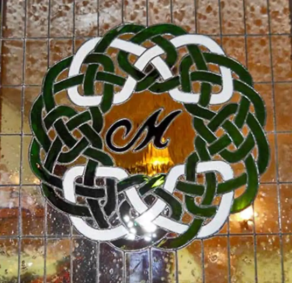 A circular green-and-white interlaced design with dark lettering is mounted on a tiled wall.