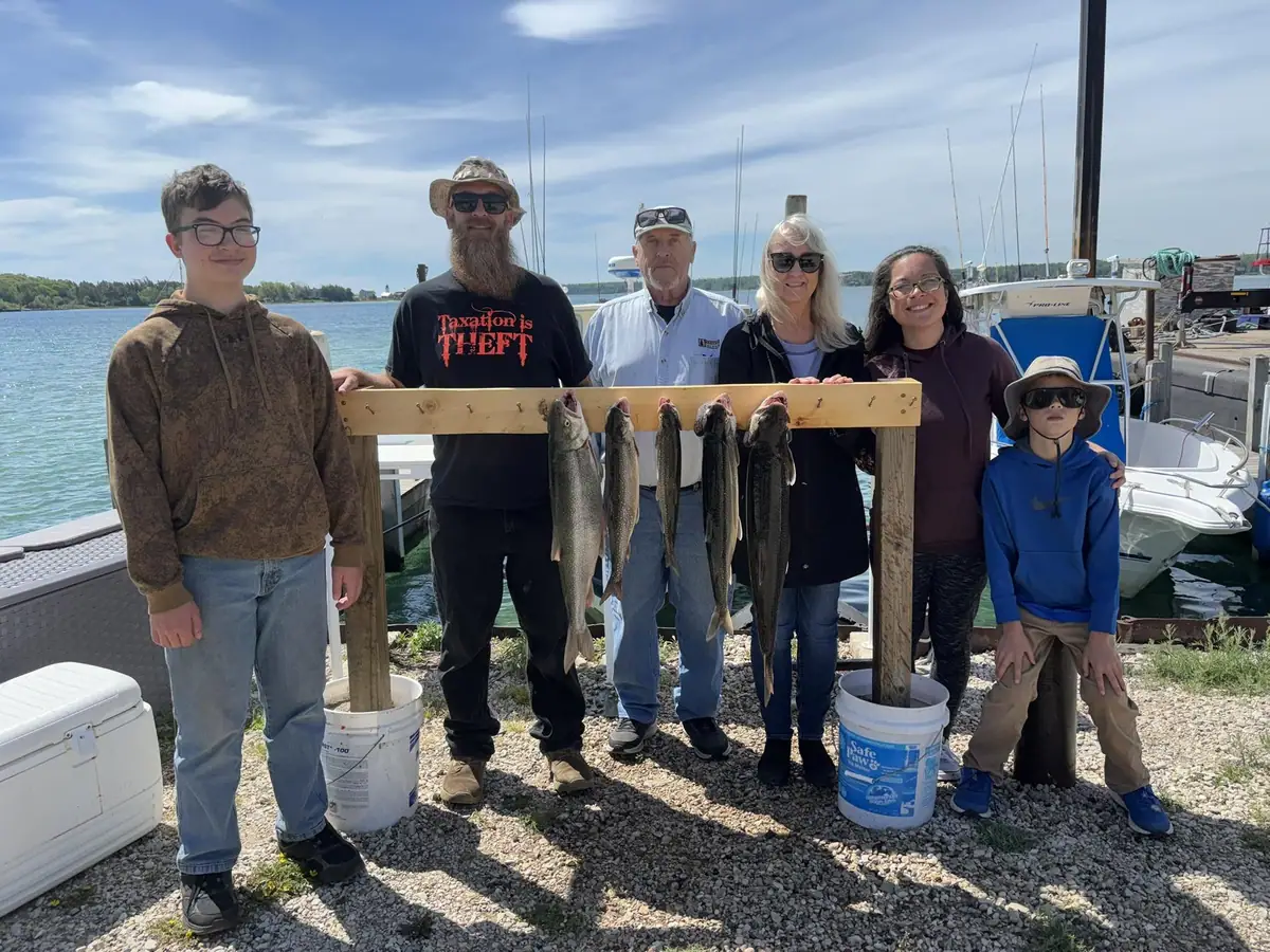 Six people pose beside a wooden rack displaying several large fish at a waterfront dock.