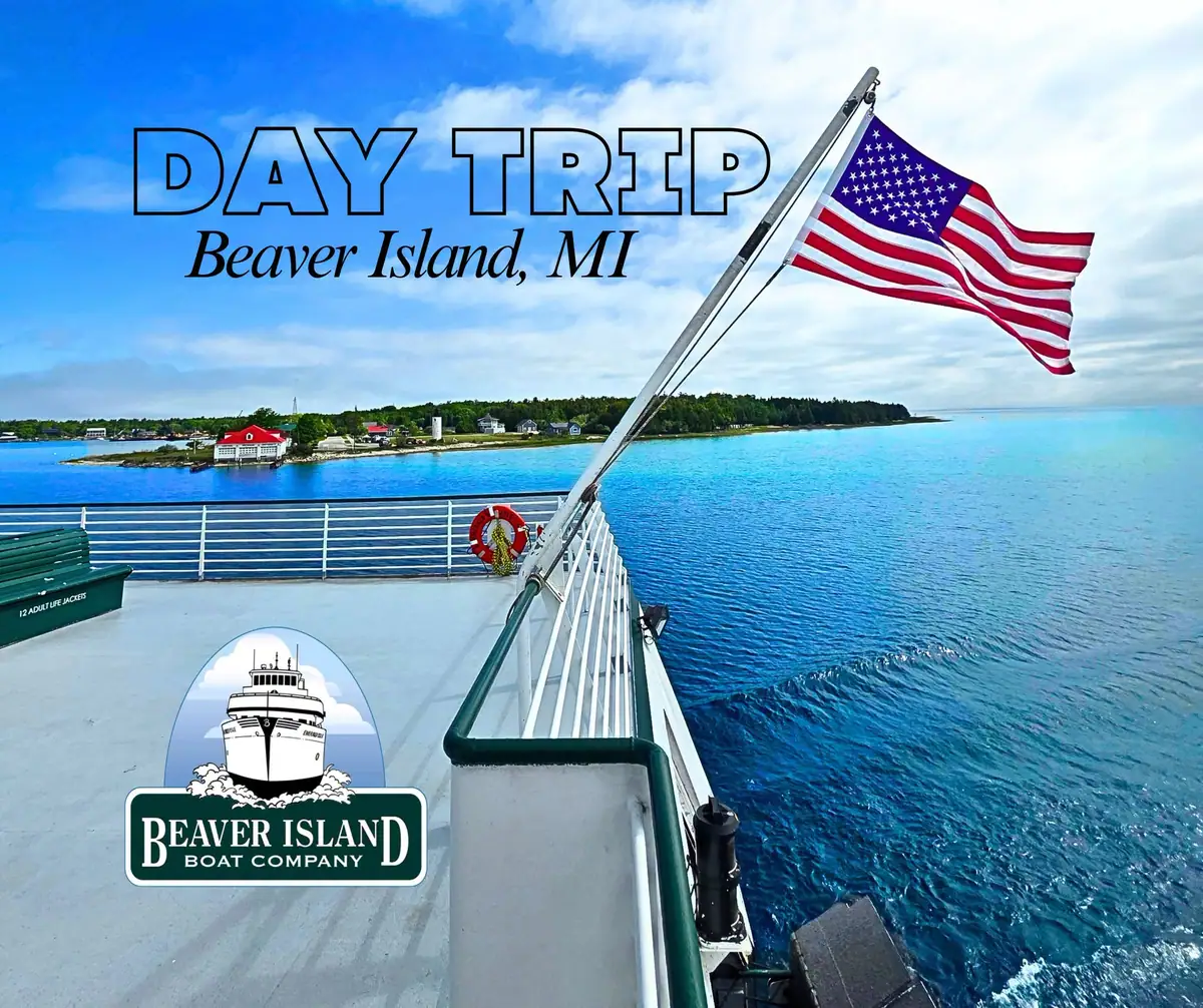 Passenger vessel deck with an American flag, blue water, and a wooded shoreline beyond.