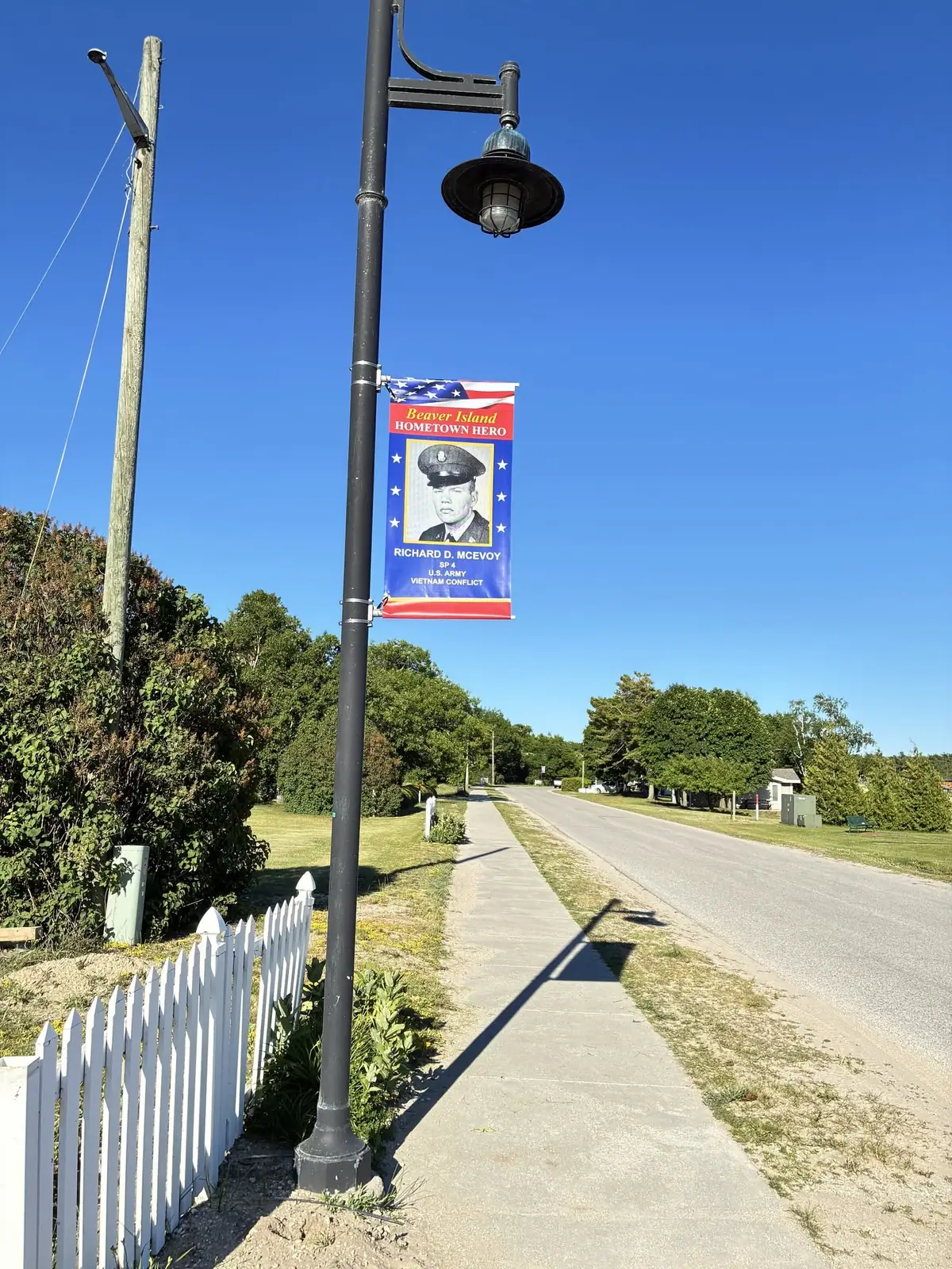 A commemorative military banner hangs from a streetlamp beside a sidewalk and road.