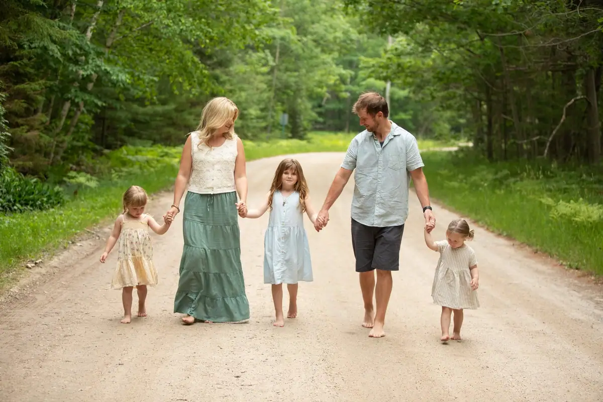 Two adults and three children walk barefoot along a wooded dirt road.