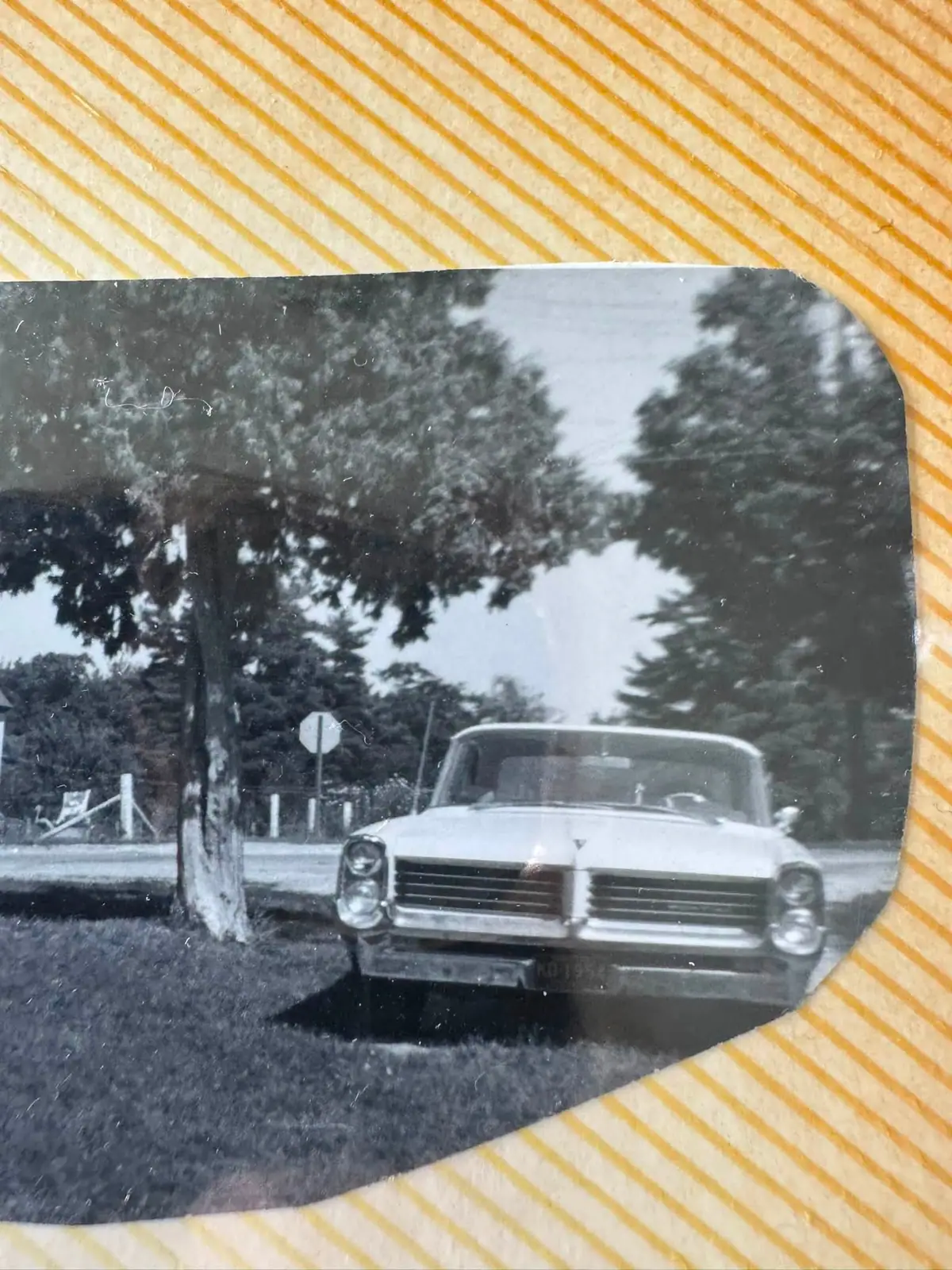 Black-and-white photograph of a vintage automobile beside a road, displayed against a yellow-and-white striped background.