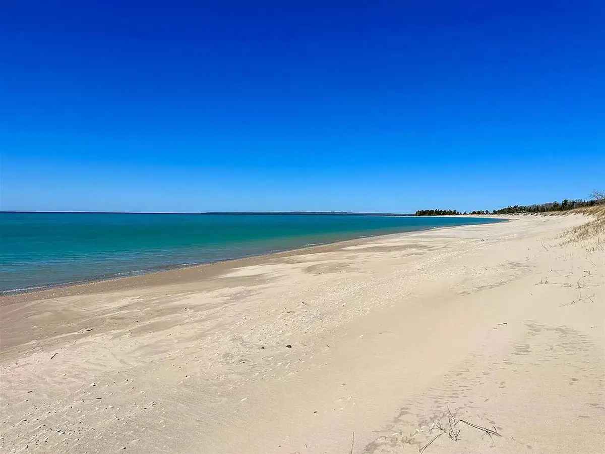 A broad sandy shoreline curves beside calm turquoise water beneath a clear blue sky.