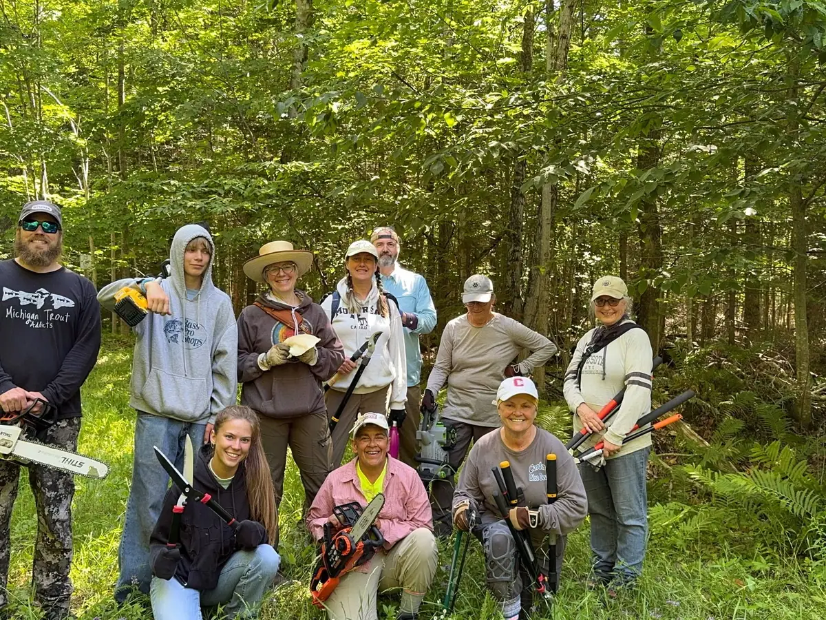 Ten people pose among trees while holding chainsaws and other tools.