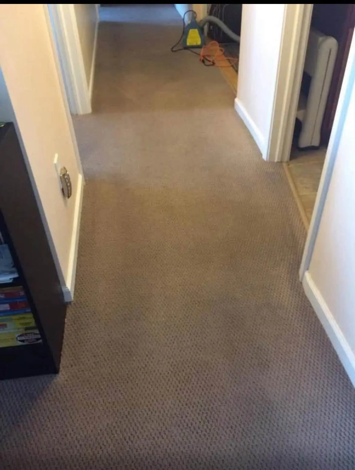 Carpeted hallway with a blue-and-yellow vacuum and orange extension cord near an open doorway.