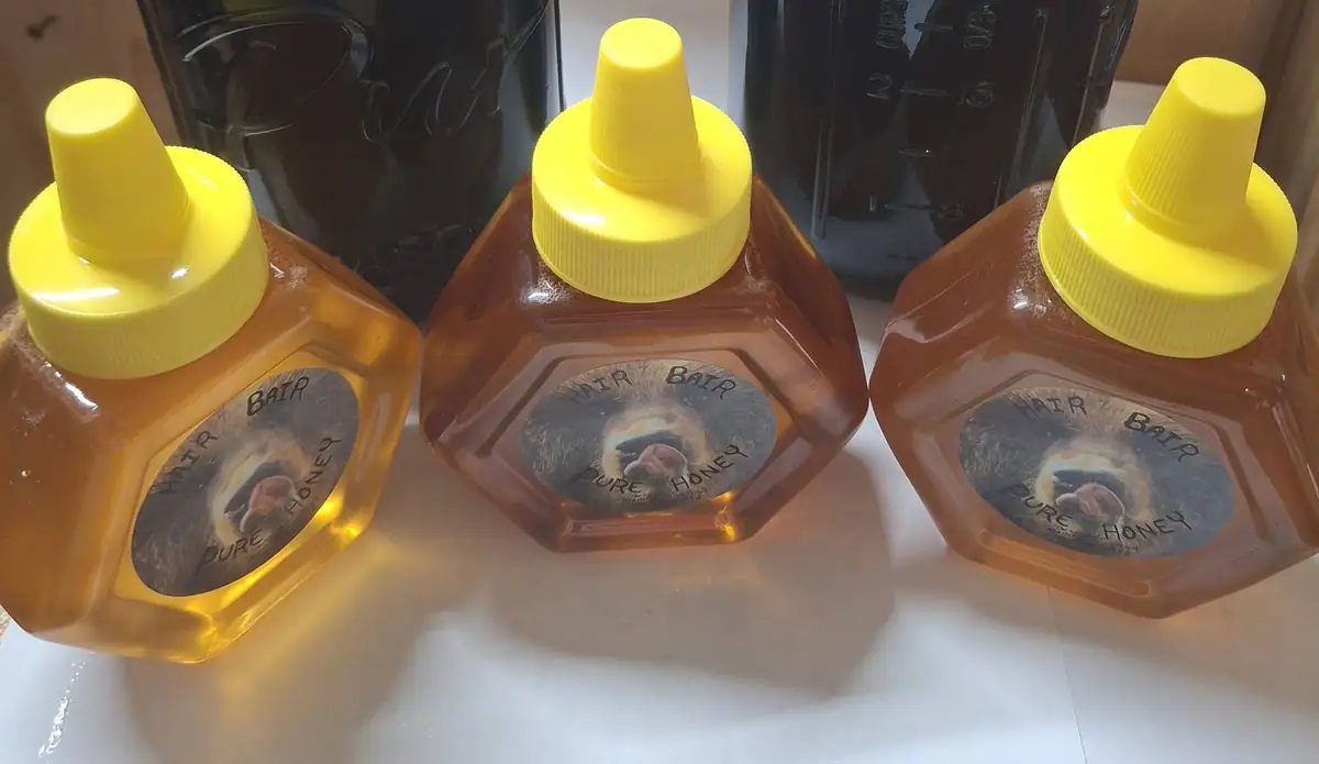 Three amber-colored honey bottles with yellow caps and bear-image labels sit on a light surface.