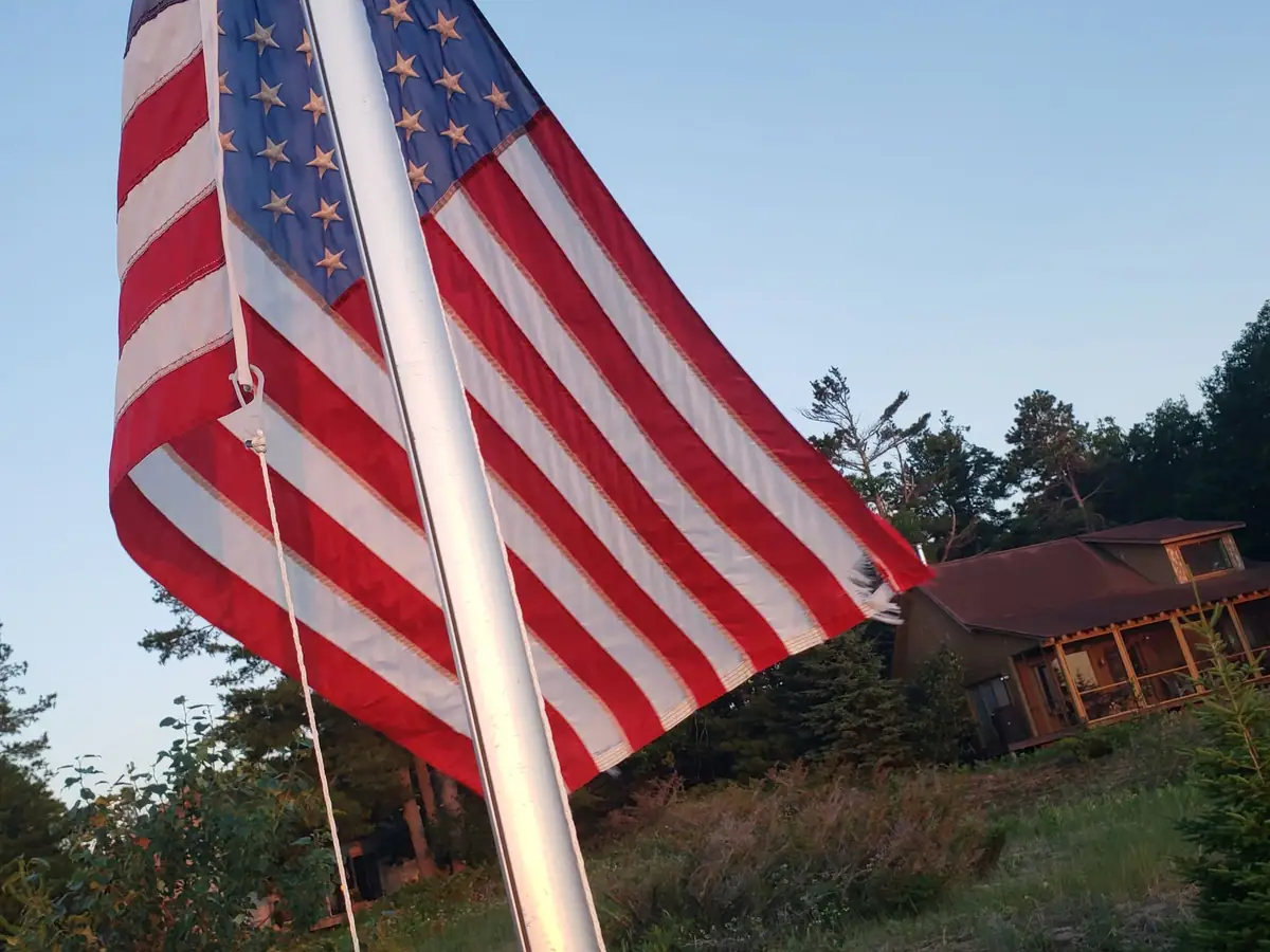 American flag on a pole beside a wooded cabin.