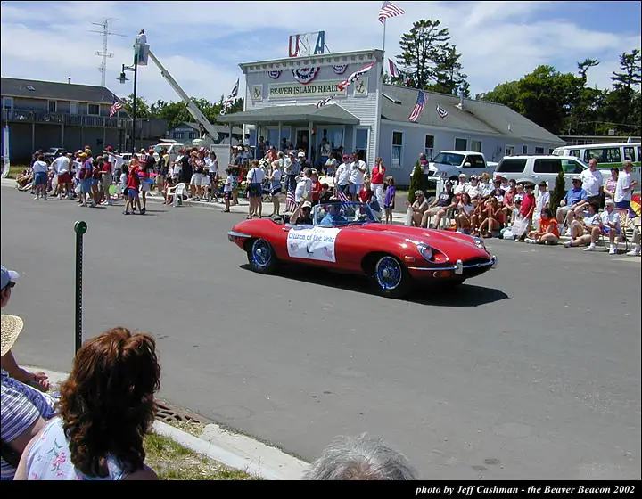 A red convertible carrying a “Citizen of the Year” banner passes spectators during a decorated street parade.