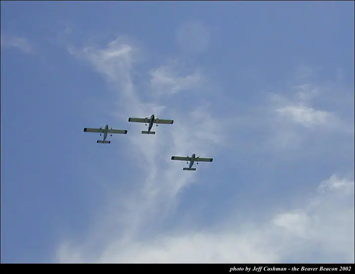 Three small green aircraft fly in formation beneath wispy clouds.