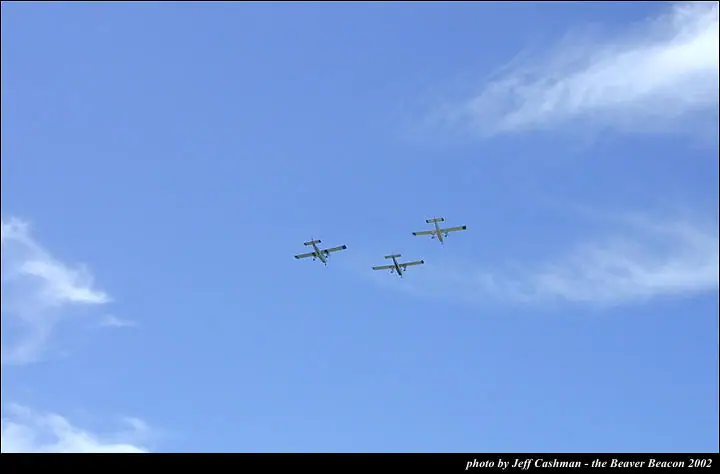 Three small propeller airplanes fly in formation against a blue, cloud-streaked sky.