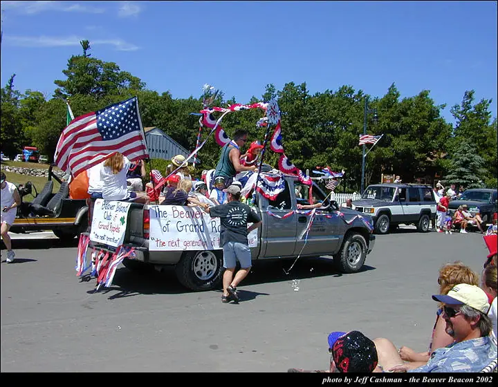 Decorated pickup truck carrying people and flags in a street parade.