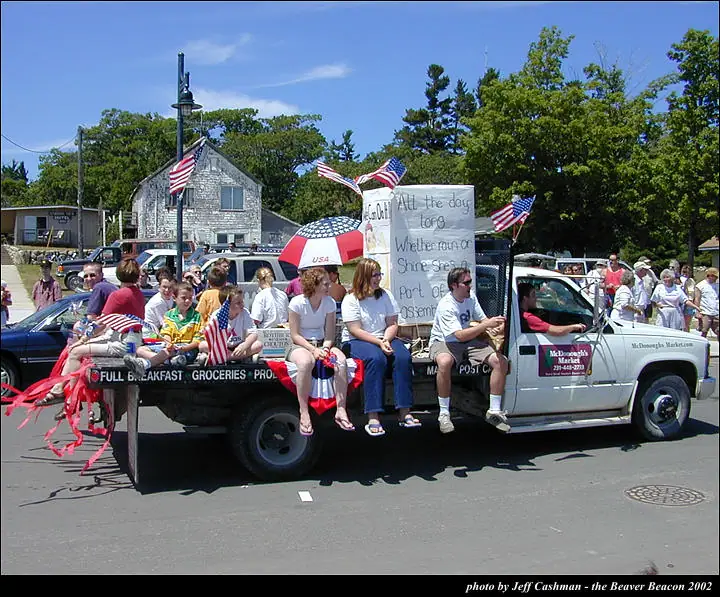 A decorated pickup truck carries people, flags, streamers, and hand-lettered signs in a street parade.
