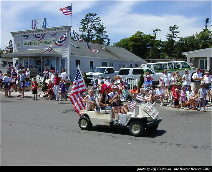 Children ride a flag-decorated parade float past a real estate office as spectators watch.