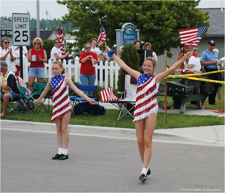 Two girls in patriotic costumes perform with a jump rope during a street parade as spectators watch.